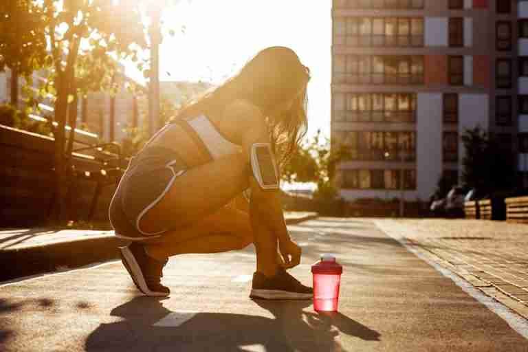 A woman preparing for a workout outdoors during the golden hour, tying her shoes on a city street.