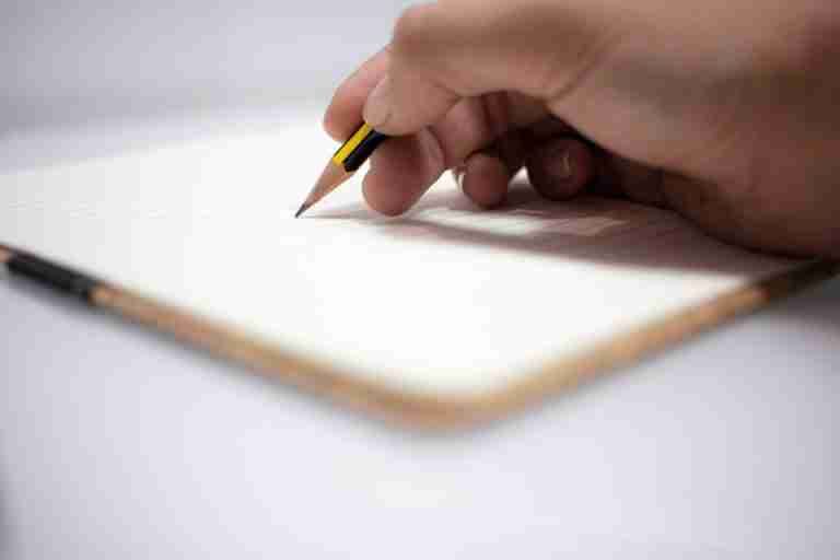 Detailed shot of a hand writing with a pencil in an open notebook, conveying creativity and focus.