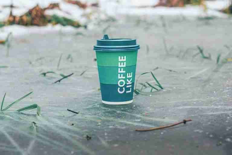 Eco-friendly coffee cup on icy surface with winter backdrop, perfect for a chilly coffee break.