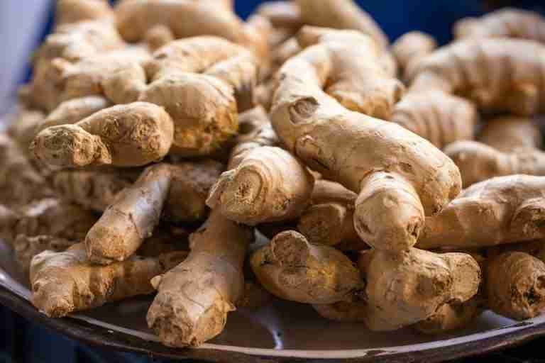 A close-up photo of fresh, raw ginger roots piled on a plate. Perfect for culinary use.