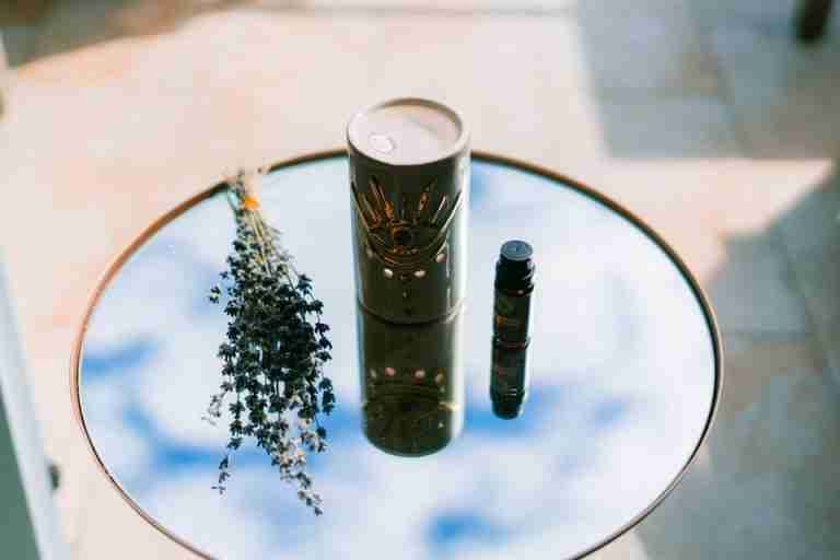 Aromatic setup with essential oil, lavender, and decorative vase reflecting in a mirrored surface outdoors.