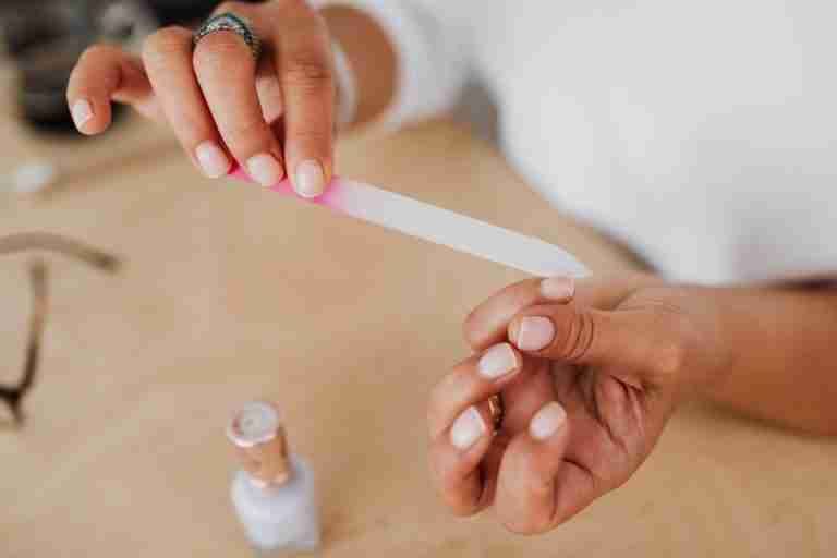 Detailed view of hands filing nails with a nail polish bottle nearby, showcasing personal grooming.