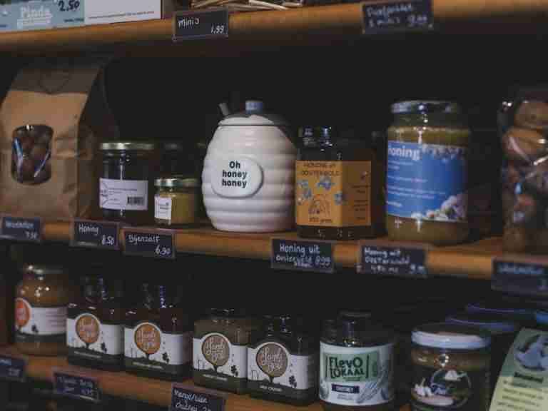 Explore artisanal honey jars and local products neatly displayed on wooden shelves in a charming Dutch shop.