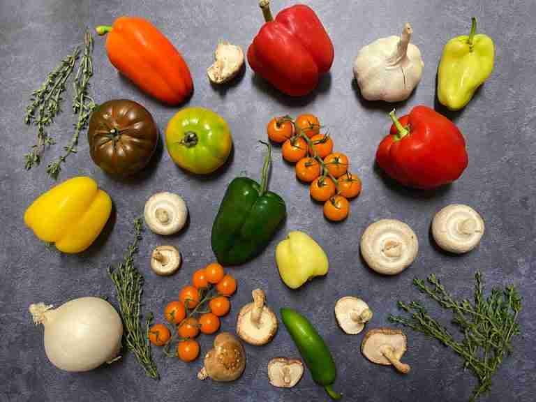 Vibrant array of fresh vegetables like peppers, tomatoes, and mushrooms in flatlay style.