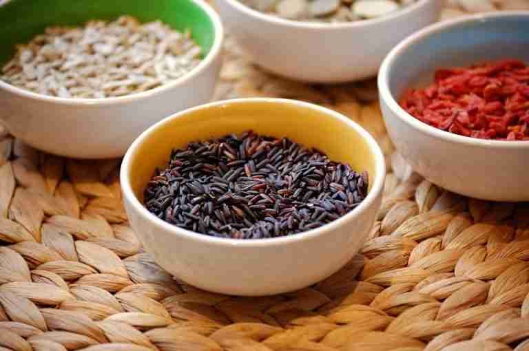 Close-up of black rice and assorted seeds in ceramic bowls. Perfect for healthy eating themes.