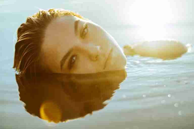 A serene portrait of a woman relaxing in the calm water with sunlit reflections creating a peaceful ambiance.