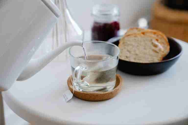 Close-up of hot water being poured into a teacup next to sliced bread on a table.
