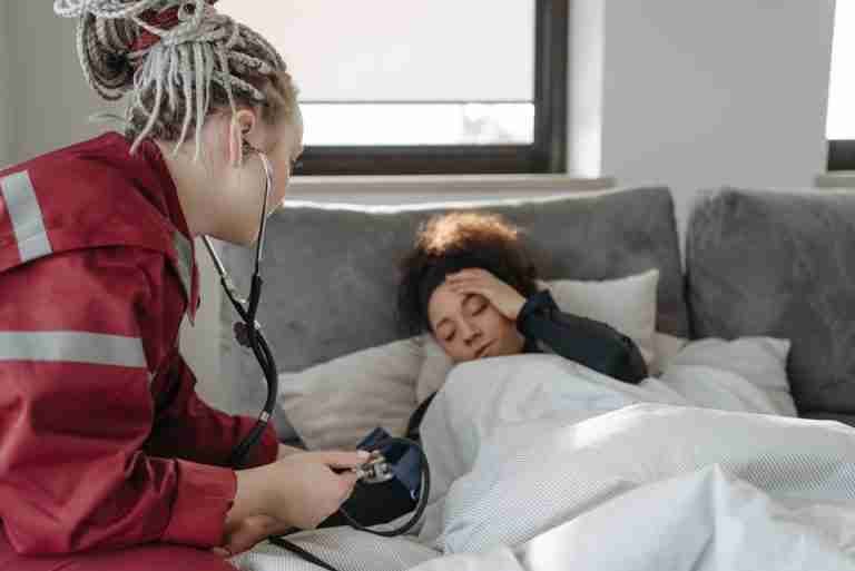 A paramedic examines a sick woman with a stethoscope indoors, providing medical care.