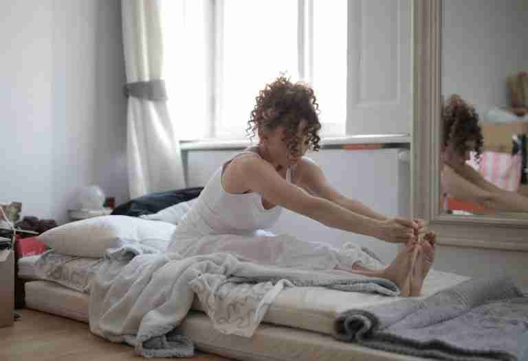 A woman in a relaxing home setting practices stretching exercises on her bed, promoting a healthy lifestyle.