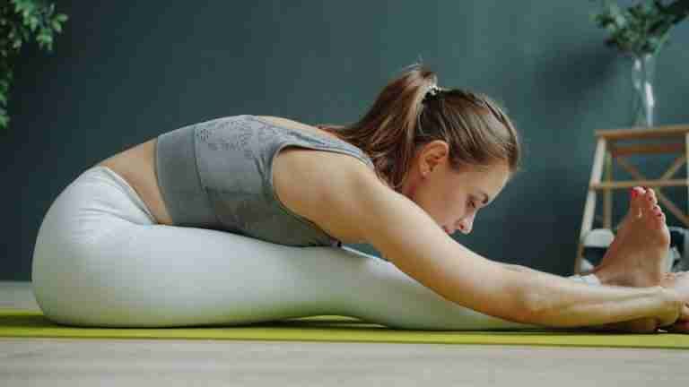 A woman in activewear stretching on a yoga mat indoors, focusing on wellness and fitness.