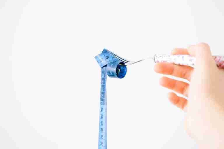 A blue measuring tape wrapped around a fork representing dieting or healthy eating concept.