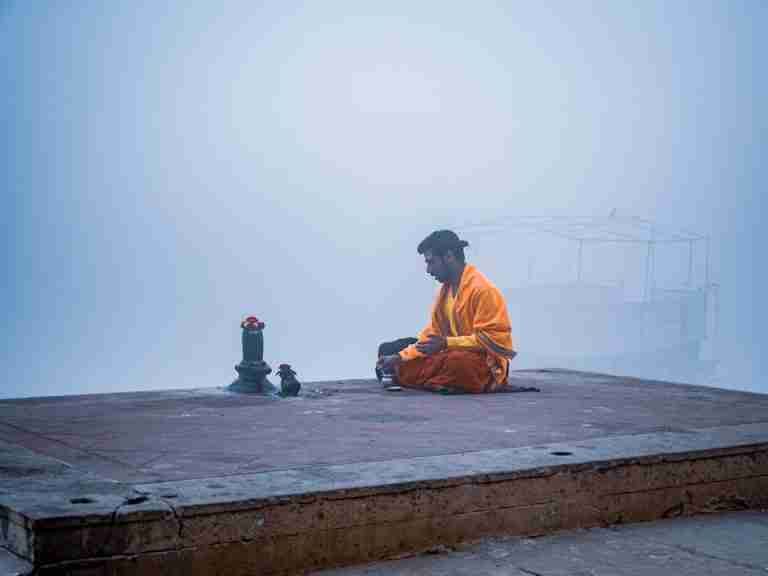 A Hindu monk meditates in solitude on a misty morning by the Ganges River in Varanasi, India.