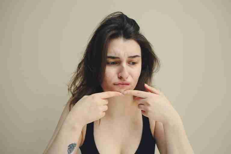 A woman looks at her skin with concern, touching her chin, worried about acne.