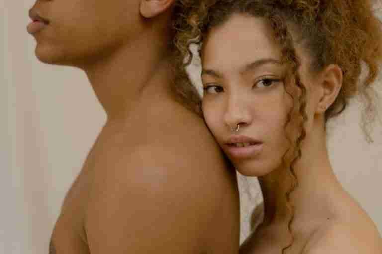 Close-up artistic portrait of two diverse young adults with curly hair and septum piercings.