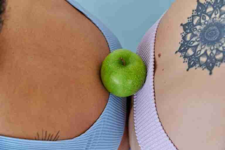 Close-up of two backs with tattoos, featuring a green apple between them, symbolizing balance.