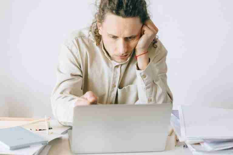 Adult man stressed at work, experiencing burnout while working on laptop at desk.