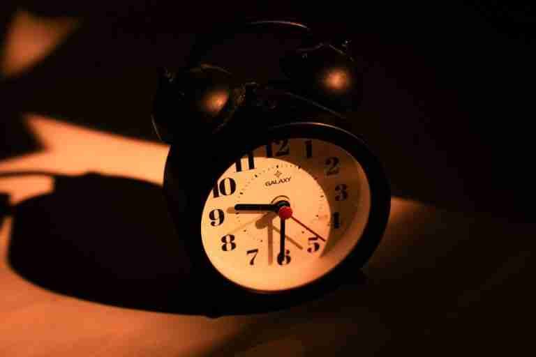 Old-fashioned black alarm clock casting a dramatic shadow under warm lighting.