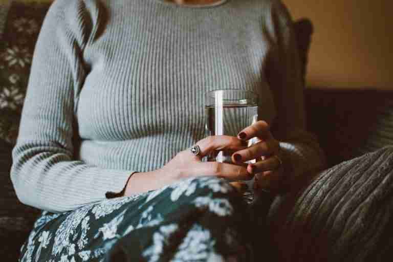 Close-up of a woman holding a glass of water while sitting indoors, conveying calm and relaxation.