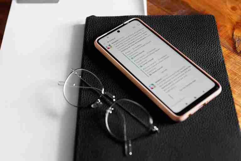 Smartphone displaying chat app on desk with notebook and eyeglasses. Ideal for technology and communication themes.