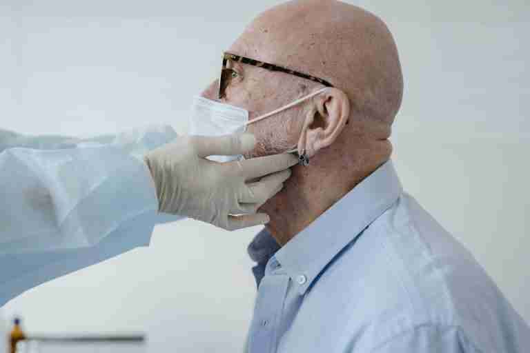 Side view of bald man with glasses wearing a face mask during a medical checkup.