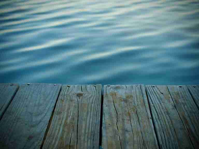 Serene image of a wooden dock leading to calm, rippling blue water, ideal for relaxation themes.