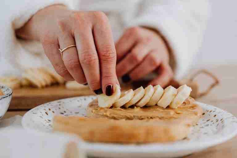 A hand places banana slices on peanut butter toast, highlighting a healthy snack preparation.