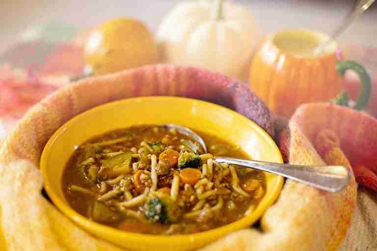 A comforting bowl of vegetable noodle soup surrounded by cozy autumn decor, perfect for a warm and hearty meal.