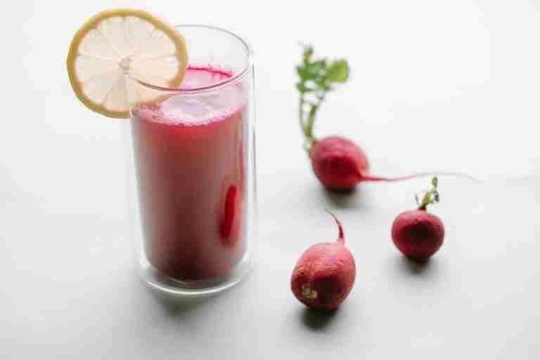 From above of glass of fresh radish smoothie decorated with piece of lemon on white background