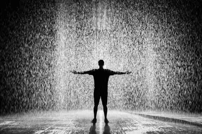 A person joyfully standing in the rain with arms wide open in a dramatic black and white scene.