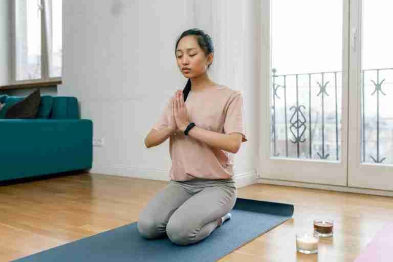 A woman practicing meditation and relaxation indoors on a yoga mat, promoting a healthy lifestyle.