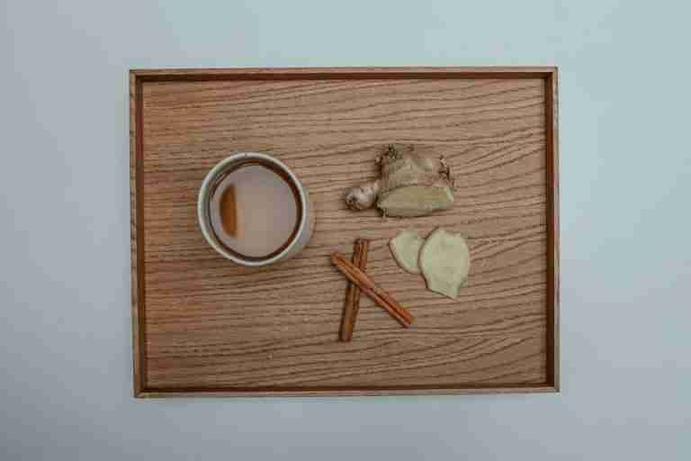 Flat lay image of a cup of tea with cinnamon sticks and fresh ginger on a wooden tray.