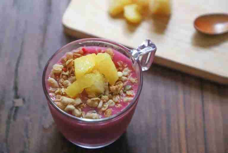 Top view of a vibrant smoothie bowl with pineapple chunks and granola on a wooden table.