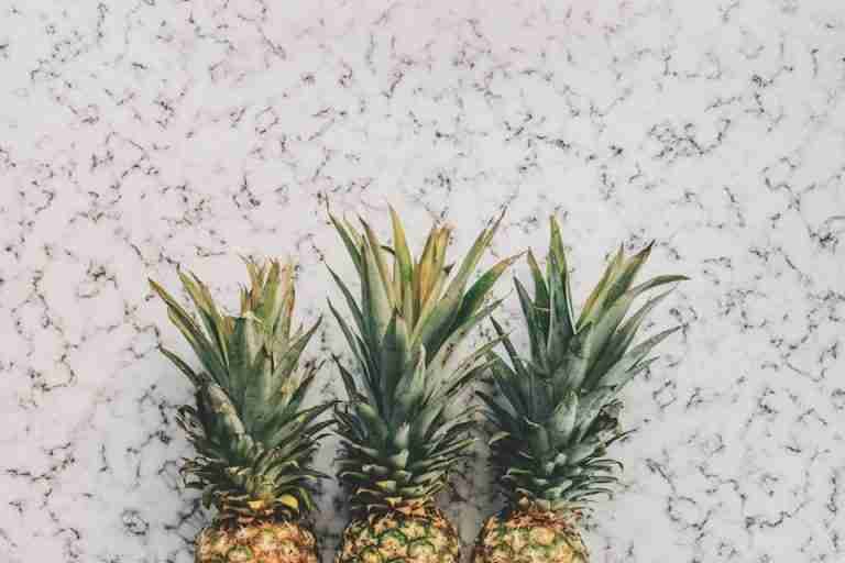 Top view of three ripe pineapples on a stylish marble surface, perfect for a tropical vibe.