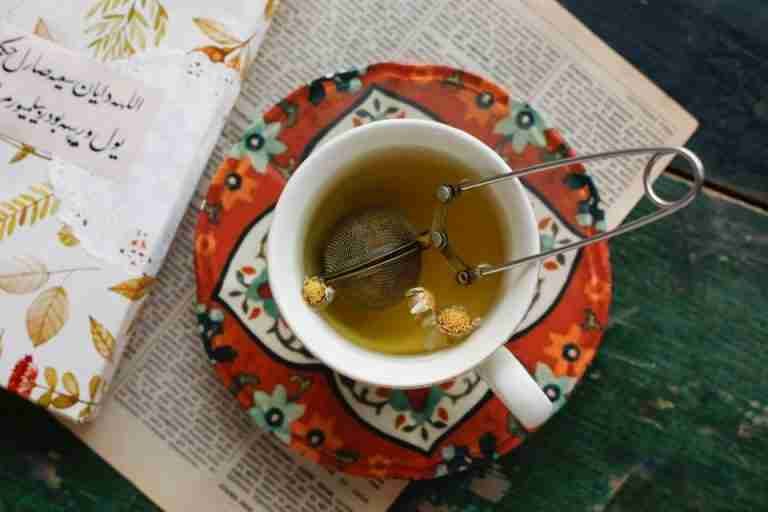A cup of herbal tea with an infuser on a vibrant floral saucer, perfect for relaxation.