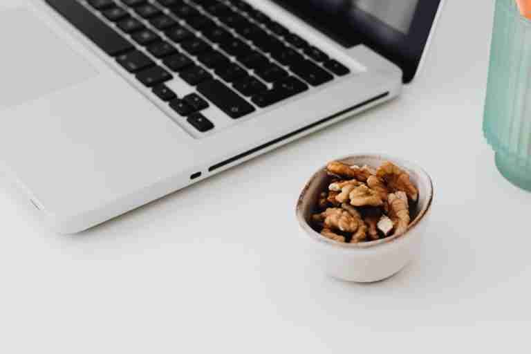 A minimalistic work desk setup featuring a laptop and a bowl of healthy walnuts for snacking.