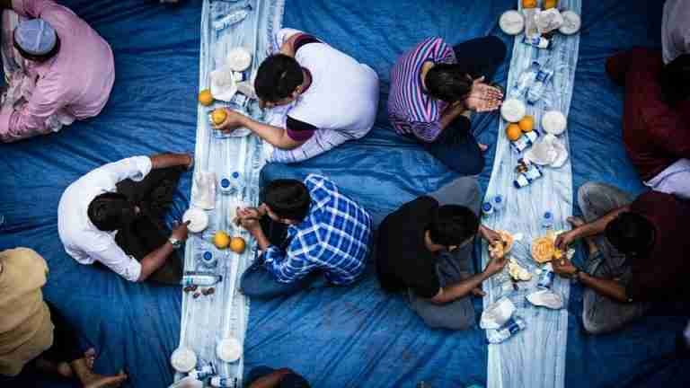 Top view of a group enjoying Iftar meal on blue fabric during Ramadan fasting period.