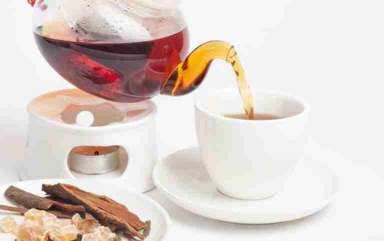 Aromatic herbal tea being poured into a porcelain cup, accompanied by cinnamon and rock sugar.