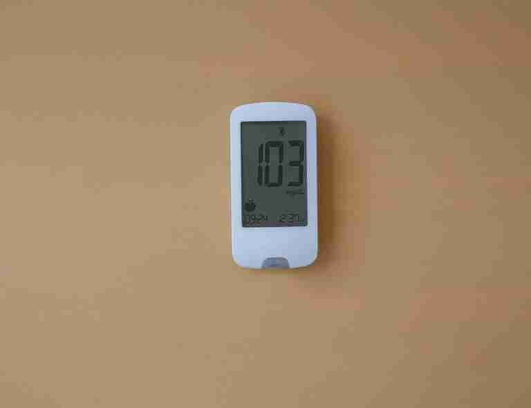 A digital glucose meter displaying blood sugar level on a beige background, ideal for healthcare themes.