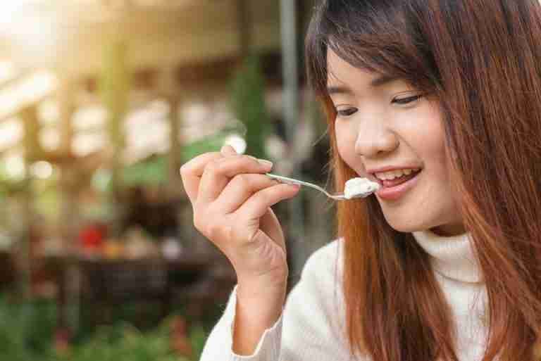 Happy woman enjoying a creamy dessert in a sunlit outdoor setting.